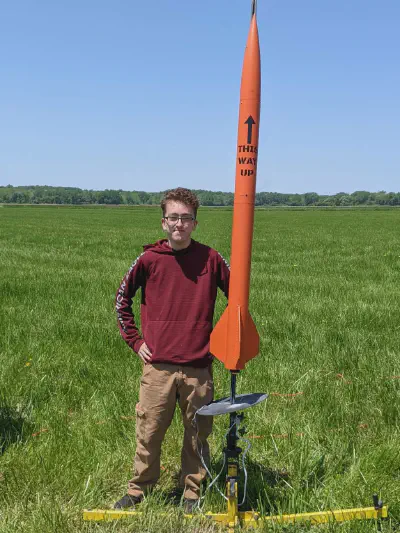 Myself standing next to a bright orange rocket called "THIS WAY UP" that is on a launch rail